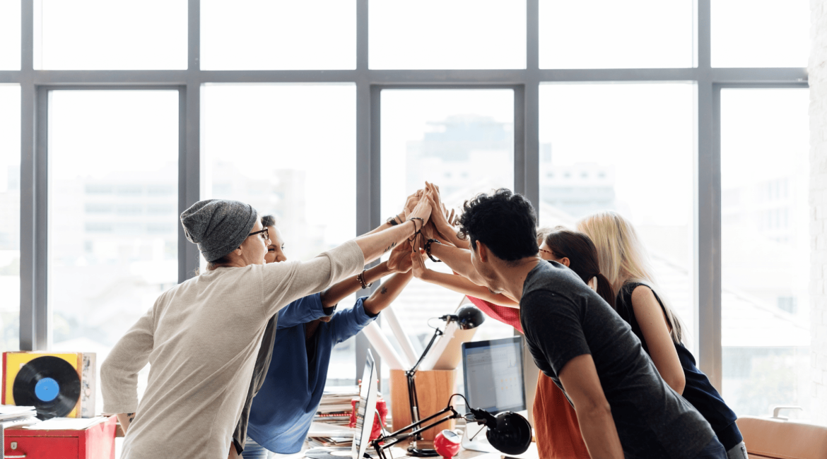 A group of young professionals giving a high five in a modern office, symbolizing teamwork, leadership, and strong workplace relationships.