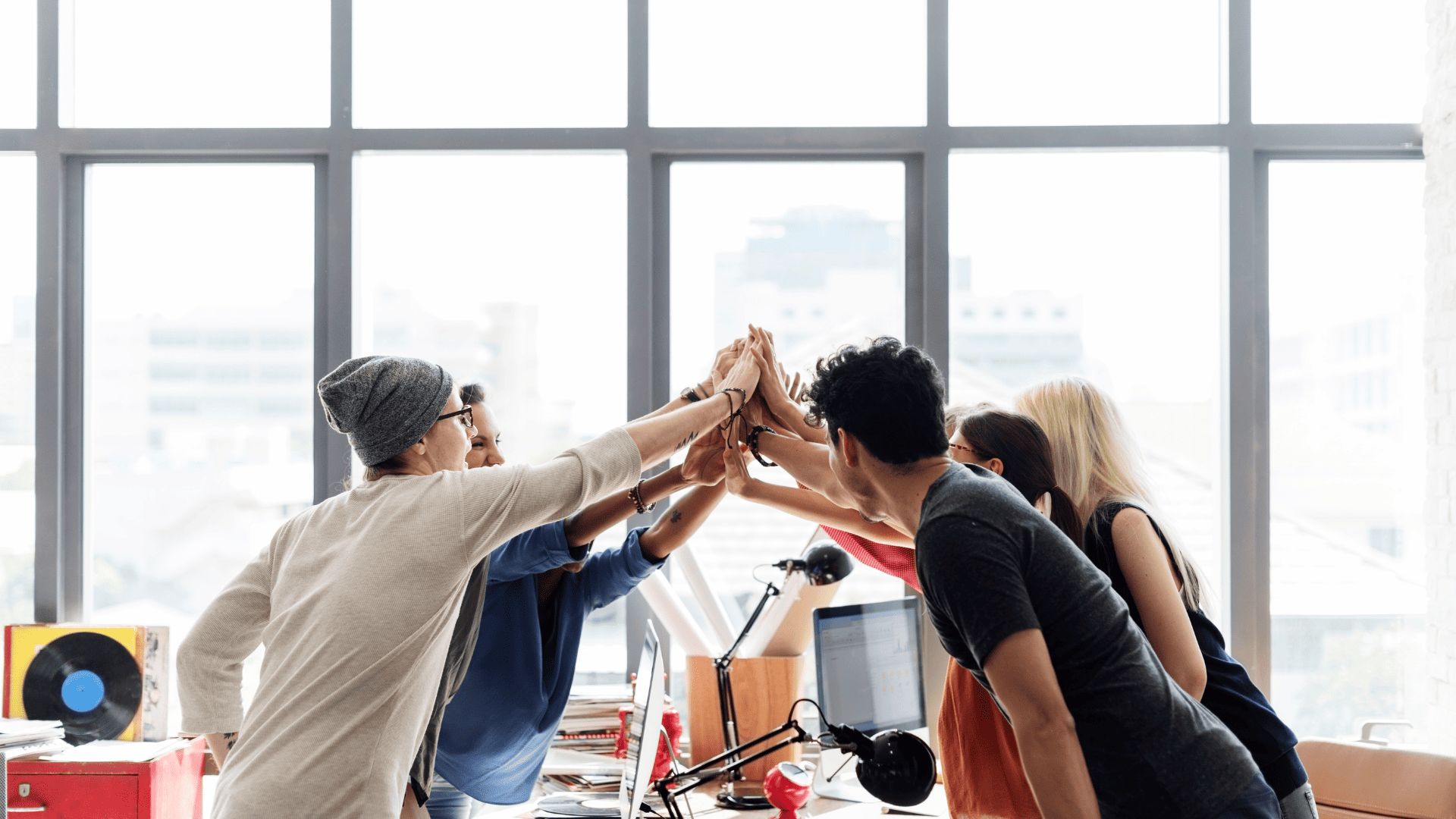 A group of young professionals giving a high five in a modern office, symbolizing teamwork, leadership, and strong workplace relationships.