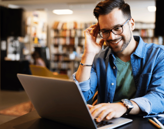 Smiling man wearing glasses working on a laptop at a desk.